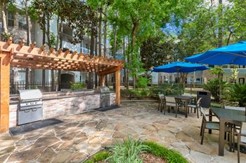 A patio with a grill and chairs under a pergola.